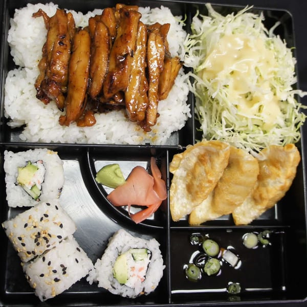 Niko Teriyaki bento box with teriyaki chicken, rice, sushi, gyoza, salad, and dipping sauce.