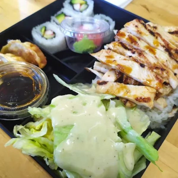 Niko Teriyaki bento box with grilled chicken, sushi, dumplings, salad, and sauces.