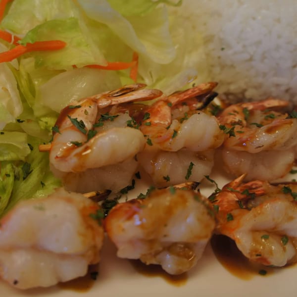 Grilled shrimp skewers with teriyaki sauce, served with a side of rice and fresh salad.