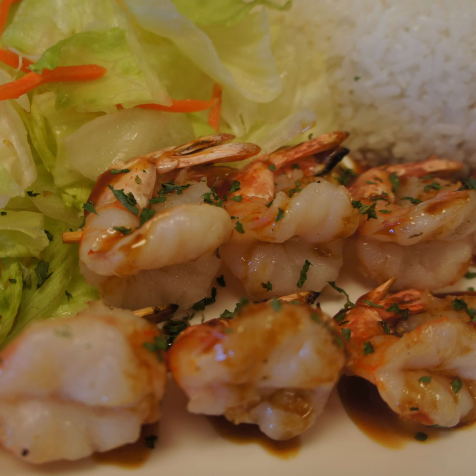 Grilled shrimp skewers with teriyaki sauce, served with a side of rice and fresh salad.