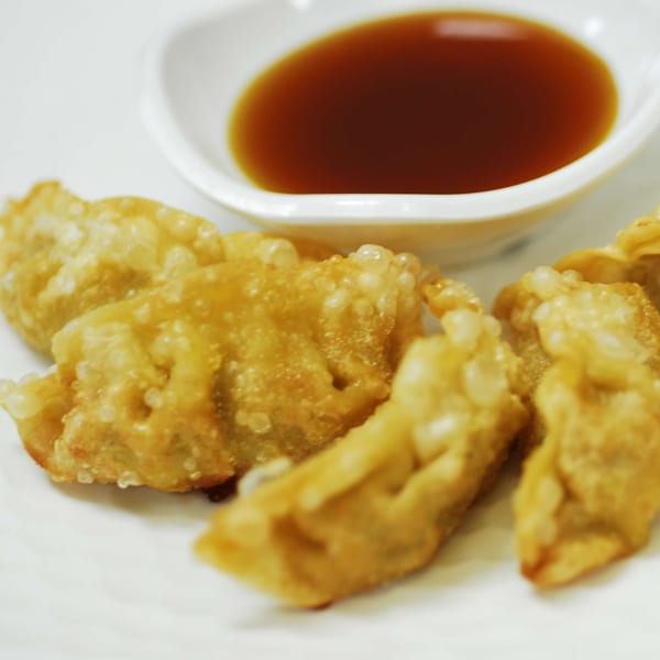 Crispy fried gyoza dumplings with a side of dark dipping sauce on a white plate.